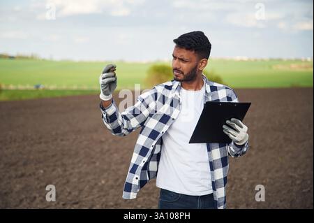 Boden in der Hand halten. Ein hübscher Indianer ist auf dem Ackerfeld. Stockfoto