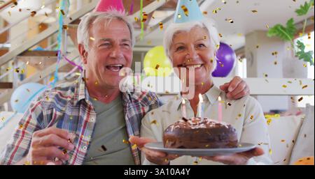 Geburtstagsfeier mit Kuchen und Kerzen, älteres Paar umgeben von Konfetti-Bild Stockfoto