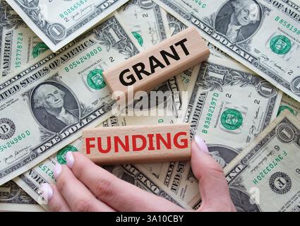 Symbol "Finanzierung gewähren". Holzblöcke mit den Worten Grant Funding. Wunderschöner Dollar-Hintergrund. Geschäftsmann Hand. Konzept für die Finanzierung von Unternehmen und Zuschüssen. Kopieren Stockfoto