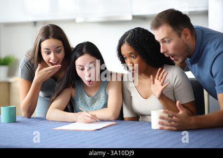 Vier überraschte Mitbewohner, die den Vertrag in der Küche zu Hause überprüfen Stockfoto