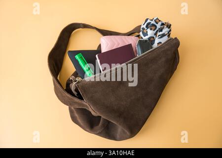 Flach liegend mit Reiseutensilien in Wildledertasche auf pastellfarbenem Hintergrund Stockfoto