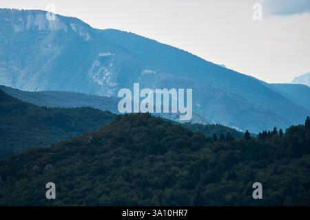 Mehrschichtige Berggipfel, bedeckt mit dichtem grünen Wald, mit Blick auf den Molvener See in den Dolomiten, Trentino, Italien Stockfoto