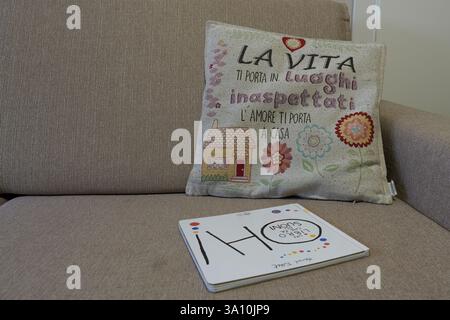 Dekoratives Kissen mit italienischem Zitat und Kinderbuch auf einem Sofa in neutralen Farben, Kalabrien, Italien. Stockfoto