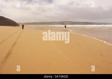 Ein Mann und eine Frau, die am riesigen Strand von Hayle am Ufer entlang laufen, in Richtung der Hayle Mündung in der Nähe von St Ives, Cornwall, England, Großbritannien Stockfoto