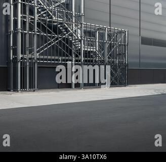 Industriegebäude außen - Notausgang: Metalltreppe an der dunkelgrauen Wand eines modernen Lagers. Stockfoto