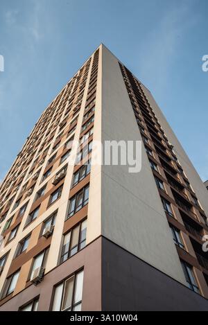 Modernes Hochhaus mit braun-beiger Fassade. Wohngebäude vor blauem Himmel bei Sonnenuntergang. Stockfoto
