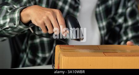 Nahaufnahme eines jungen Mannes, der ein Paket mit einem Barcode-Scanner in einem Arbeitsbereich scannt. Stockfoto