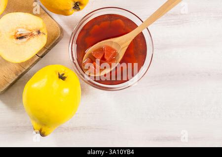 Quittenmarmelade im Glas oder in einer Schüssel mit Reifen frischen Quitten auf rustikalem Tisch, Obstmarmelade-Konzept zum Frühstück Stockfoto