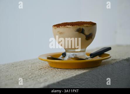 Italienisches Dessert Tiramisu in Glasbecher und Löffel auf Untertasse im sonnendurchfluteten Café. Stockfoto