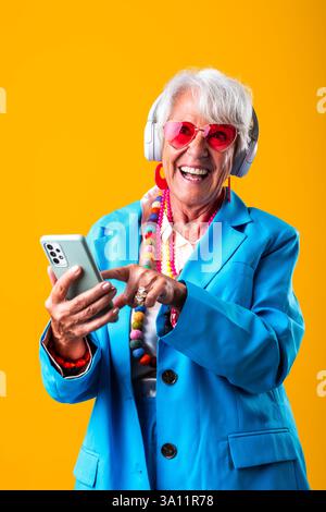 Schöne ältere Frau mit grauen Haaren, die im Studio farbenfrohe, stilvolle Kleidung trägt - fröhliche alte Großmutter mit modischem Stil Stockfoto