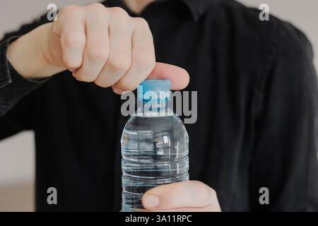 Nahaufnahme eines Mannes, der die Plastikkappe der Wasserflasche öffnet. Tägliche Wasseraufnahme. Stockfoto