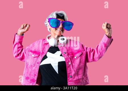 Schöne ältere Frau mit grauen Haaren, die im Studio farbenfrohe, stilvolle Kleidung trägt - fröhliche alte Großmutter mit modischem Stil Stockfoto