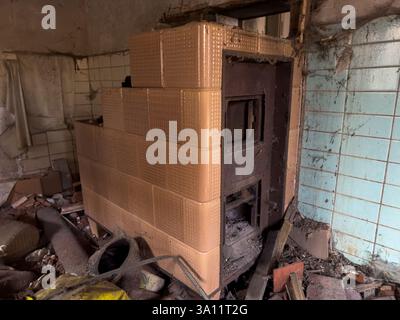 Ein alter, verlassener, zerstörter Kachelofen aus vergangenen Zeiten in einem Zimmer Stockfoto