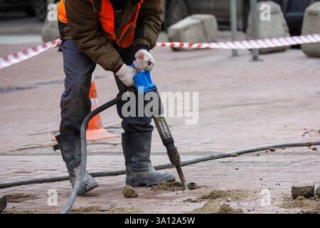 Der Arbeiter repariert die Straßenoberfläche mit einem Presslufthammer. Bauarbeiten, Verlegen von Pflasterplatten in der Stadt Stockfoto
