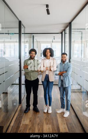 Drei selbstbewusste Geschäftsleute stehen mit überkreuzten Armen in einem modernen Büro. Ein Symbol für Teamarbeit, Führungsstärke und unternehmerische Ambitionen. Stockfoto