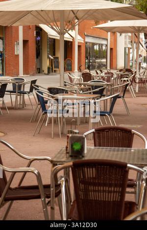 Moderne Metalltische und gewebte Stühle in einem leeren Café im Freien. Architektonische Kulisse und einladende Farben. Stockfoto