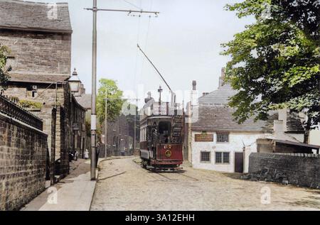 Blick nach Osten entlang der Rochdale Road in Stile, Triangle, West Yorkshire, England, Großbritannien in den frühen Jahren des 20. Jahrhunderts. Das Dorf, das im Ryburn Valley liegt, war der Endpunkt der Halifax Corporation Tramways Route 5 (Sowerby Bridge to Triangle – eröffnet am 10. Februar 1905). Auf Passagiere wartet Tramcar 67, eine Doppelstockbahn mit offenem Oberdeck, die von Brush im Jahr 1901 gebaut wurde. Auf der rechten Seite befindet sich der Blue Ball Pub. Auf der linken Seite befindet sich eine Reihe von drei Geschäften, deren Zentrum ein „Paketbüro“ war – aus dem später Triangle's Fish and Chips Shop wurde. Die Geschäfte wurden später für eine Straßenverbreiterung abgerissen. Stockfoto