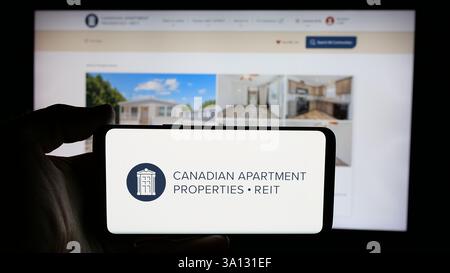 In dieser Abbildung hält eine Person ein Mobiltelefon mit dem Logo der Firma Canadian Apartment Properties REIT (CAPREIT) auf dem Bildschirm vor der Webseite. Stockfoto