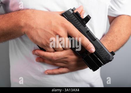 Detail eines Schießlehrers, der ein weißes Hemd trägt und einen Revolver in der Hand hält. Isoliert auf grauem Hintergrund. Sportpraxis. Brasilien Stockfoto
