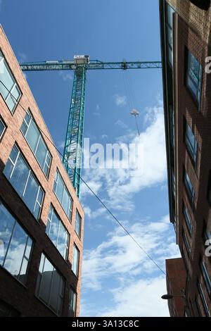 Dublin, Irland - 05. März 2025 - Ein großer Baukran, der von einem Fußweg auf der Strand Street aus gesehen wird, mit blauem Himmel und Wolken, die sich an einem sonnigen Nachmittag in Dublin spiegeln Stockfoto