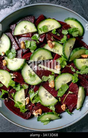Veganer Rüben-Salat. Marinierte Rote Bete in Scheiben mit frischer Gurke, Walnüssen und Korianderblättern in einer Keramikschale. Hintergrund zu Lebensmitteln. Gesund, pflanzenbasiert Stockfoto