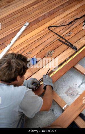 Ein Handwerker misst und richtet Holzdielen sorgfältig aus, während er ein Deck baut. Er verwendet Werkzeuge wie ein Maßband und eine Ebene, um die Genauigkeit zu gewährleisten. Haben Sie jemals W Stockfoto