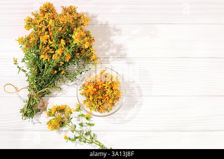 Sammlung nützlicher Kräuter zur Behandlung nach Volksrezepten. Blumenstrauß aus frischen Hypericum-Blüten und getrockneten Blütenblättern in einer Tasse auf einem Holztisch, al Stockfoto