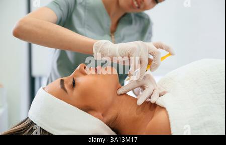 Gelbe Spritze, Herstellung der Injektion. Frauengesicht wird von Kosmetikerhänden im Spa-Salon Gesichtspflege bekommen. Stockfoto