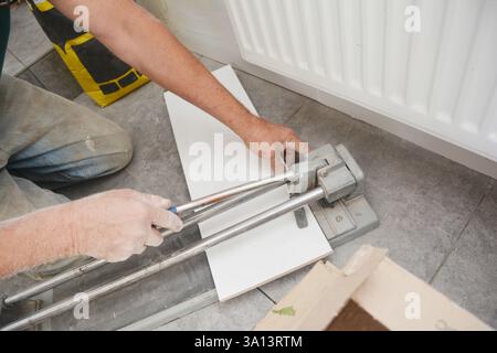 Ein Baumeister schneidet weiße Keramikfliesen während der Renovierung der Badezimmerwände. Stockfoto