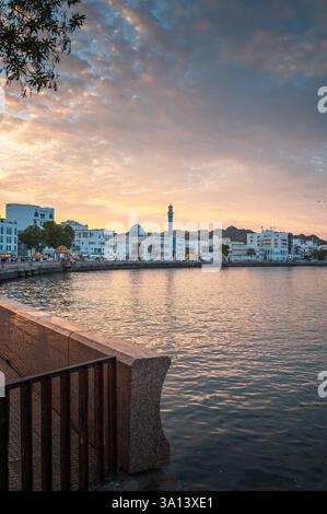 Der Sonnenuntergang wirft goldene Farbtöne über der Muttrah Corniche in Maskat, Oman, wo die Uferpromenade auf den ruhigen Golf von Oman trifft. Die Szene erfasst das c Stockfoto