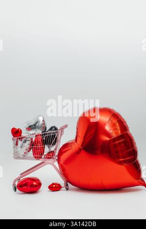 Großes rotes Herz mit rosa Wagen voller Ballons auf weißem Hintergrund. Fotozone mit Herzen für Liebhaber Stockfoto