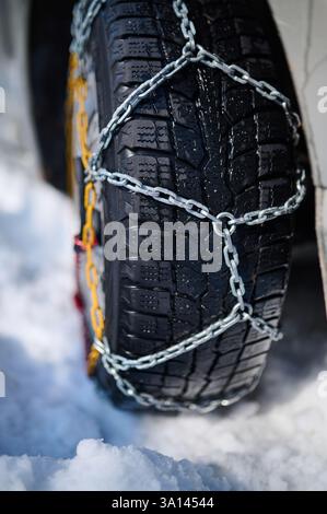Nahaufnahme eines Winterreifens mit Schneeketten für verbesserte Traktion auf vereisten und verschneiten Straßen. Die Metallglieder wickeln sich eng um die robuste Lauffläche Stockfoto