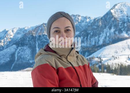 Porträt einer 45-50-jährigen Frau in einer warmen Jacke, die die frische Bergluft genießt und sich vor dem Hintergrund verschneite Berghänge posiert Stockfoto