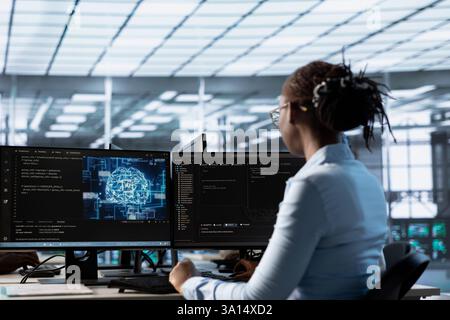Techniker, der am PC-Schreibtisch arbeitet und im KI-Serverraum recherchiert. afroamerikanischer IT-Experte untersucht Mainframes in Rechenzentren mithilfe von Computern Stockfoto