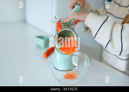 Weibliche Hand hackt Karotten auf dem Boden mit einer automatischen blauen Reibe Stockfoto