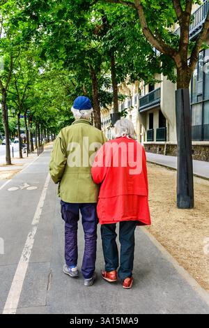 Älteres Ehepaar, das Arm in Arm auf dem von Bäumen gesäumten Boulevard spaziert - Paris, Frankreich. Stockfoto
