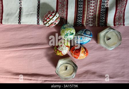 Set mit bemalten Ostereiern. Geometrisches Muster, verschiedene Farben, Ornamente auf jedem. Auf einem der Eier ist ein Vogel. Sojakerzen in der Nähe. Handtuchstickerei Stockfoto