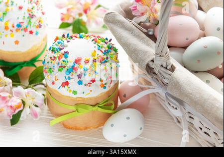 Köstliche osterkuchen mit bunten Streuseln und bemalten Eiern in einem Korb sind von Frühlingsblumen umgeben Stockfoto