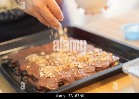 Koch, Backen und Bananenkuchen mit Penüssen und Schokolade in einer Küche von Frau, die eine süße Nachspeise oder einen Geburtstag zubereitet. Selektiver Fokus. Stockfoto