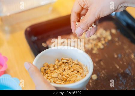 Weibliche Handbäckerin, die leckeren Kuchen mit Cashewnüssen am Tisch dekoriert. Hausgemachtes süßes Konzept. Seitenansicht, selektiver Fokus. Stockfoto