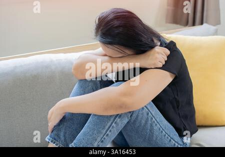 Asiatische Frau mit Stress, sie hielt sich allein auf dem Sofa im Wohnzimmer, verärgerte einsame reife Frau. Depressionskonzept. Stockfoto