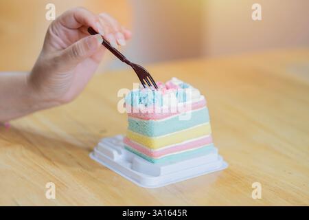 Nahaufnahme einer Frauenhand, die einen Paarbogenkuchen in Plastiktablett über Holztisch im Café isst. Selektiver Fokus. Stockfoto