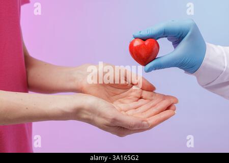 Ein medizinischer Fachmann in blauen Handschuhen übergibt einem Patienten ein rotes, herzförmiges Objekt, das Organspende, Herzgesundheit und medizinische Versorgung symbolisiert Stockfoto