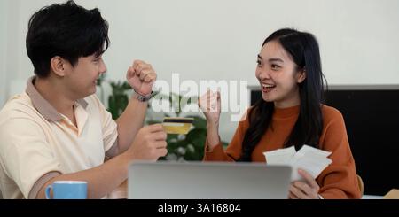 Verbinden Sie die Verwaltung von Finanzen. Junges Paar begeistert von finanziellen Entscheidungen zu Hause, diskutiert Pläne und feiert gemeinsam. Stockfoto
