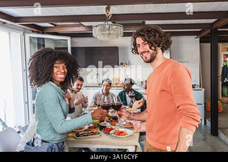 Verschiedene Freunde genießen eine Mahlzeit und toasten Rotwein, feiern Freundschaft und Zweisamkeit zu Hause Stockfoto