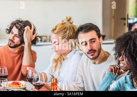 Eine Gruppe verschiedener Freunde genießt gemeinsam ein Abendessen und führt zu Hause ein interessantes Gespräch Stockfoto