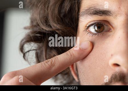 Nahaufnahme des Gesichts eines jungen Mannes, während er die Haut unter seinem Auge berührt und auf Falten, dunkle Kreise oder andere Unregelmäßigkeiten untersucht Stockfoto