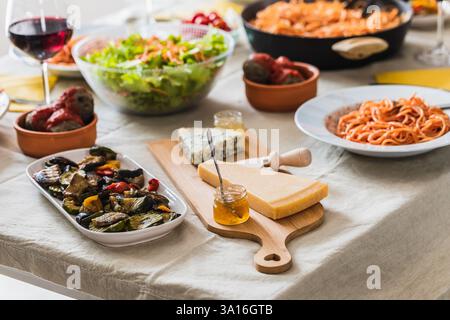 Köstliche italienische Küche mit Pastagerichten, frischem Salat, gegrilltem Gemüse und einer Auswahl an Käsesorten mit Honig, die eine lebhafte und inviente Atmosphäre schaffen Stockfoto