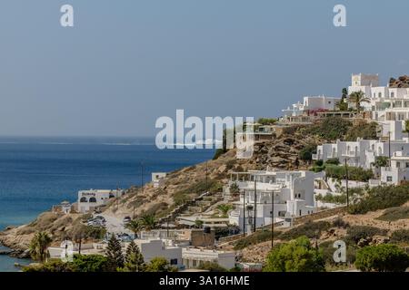 IOS, Griechenland - 6. September 2024 : Blick auf ein schönes weiß getünchtes Hotel, ein Restaurant und ein Fährschiff im Hintergrund in iOS Griechenland Stockfoto