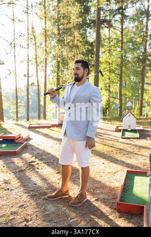 Porträt eines jungen erwachsenen Minigolfspielers mit Schläger auf dem Platz im Wald Stockfoto